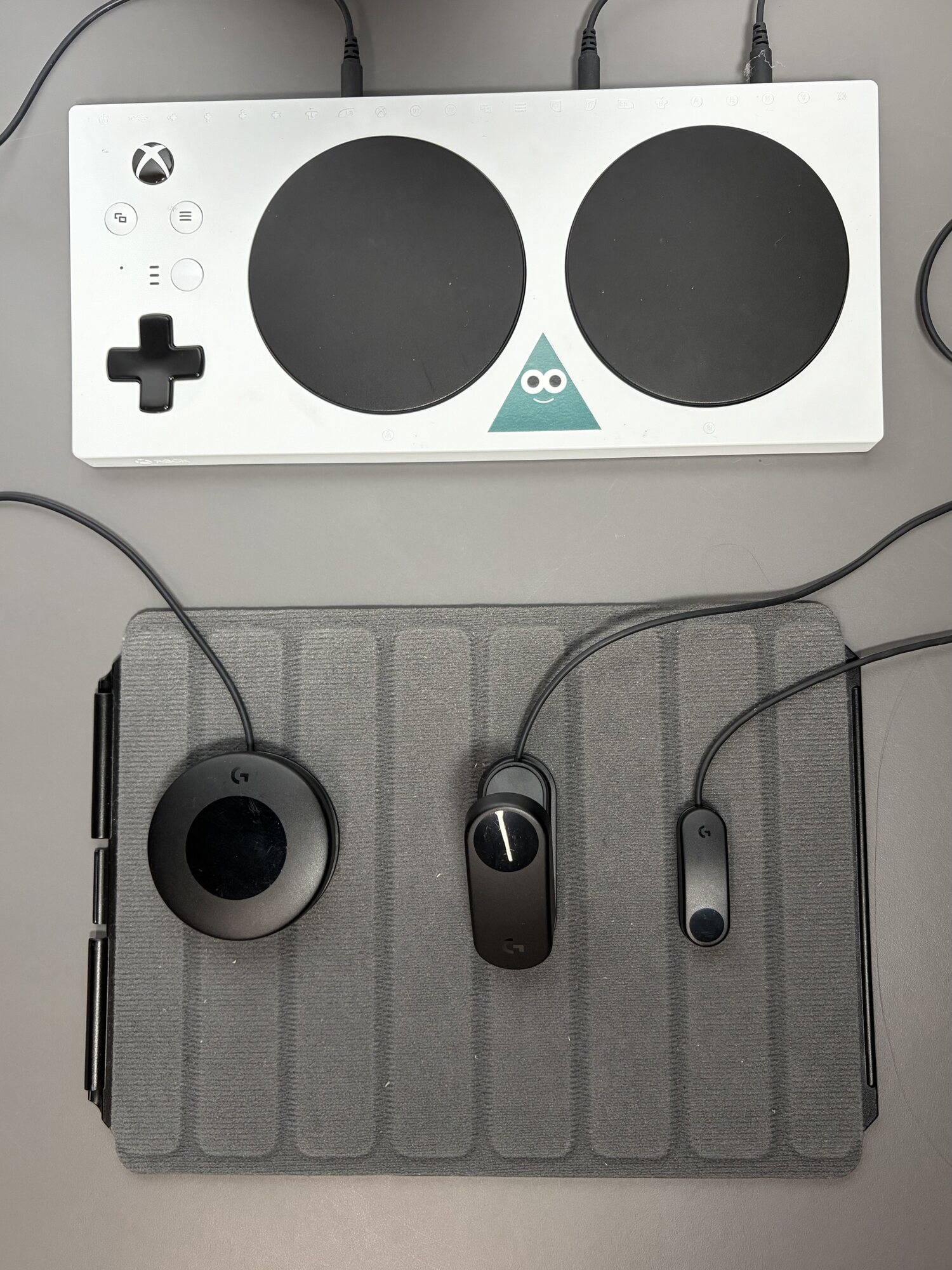 Xbox Adaptive Controller أبيض وثلاثة مفاتيح خارجية موصولة على بساط تثبيت رمادي